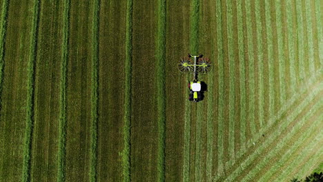 Super-wide-aerial-drone-shot-zooming-in-a-tractor-with-an-rotating-equipage-collecting-dried-mowed-grass-on-a-large-green-field