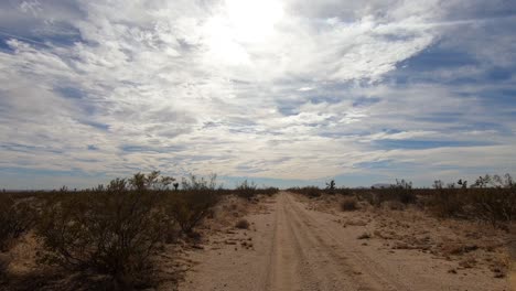 Driver-POV-driving-on-dirt-path-in-Mojave-Desert-toward-cloudy-sky