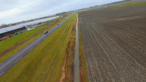 Aerial-shot-going-from-a-small-road-to-the-main-road-surrounded-by-farm-fields