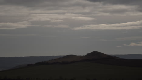 Low-gray-clouds-cast-shadows-over-lonely-hill,-time-lapse