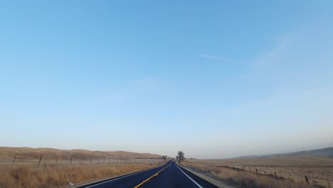 Driving-on-road-through-sprawling-yellow-grasslands-in-changing-season