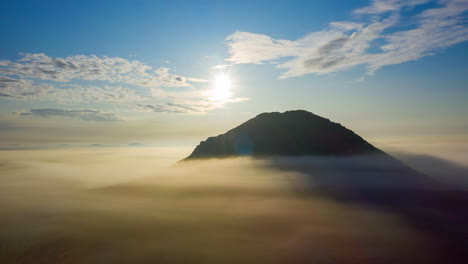 Flying-above-golden-fog-with-mountain-peak-visible-in-bright-sun,-Hyperlapse