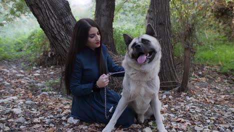A-woman-and-her-dog-sit-in-the-forest-as-she-lovingly-caresses-her-happy-Akita