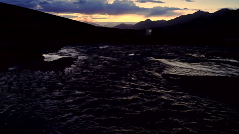 Dark,-gloomy-sunset-shot-late-evening-in-the-mountains-with-orange-and-blue-sky-and-a-river-in-the-foreground