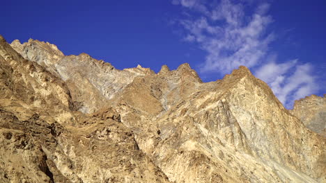 Pan-right-over-a-bald-mountain-range-top,-peaks-with-blue-sky-on-a-sunny-day