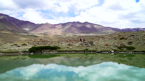 People,-hikers-walking-on-the-Markha-Valley-trek-near-to-a-lake,-that-calm-water-reflecting-the-landscape