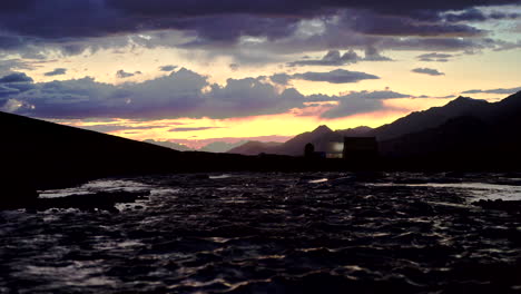 Handaufnahme-Eines-Erstaunlichen-Sonnenuntergangs-In-Den-Bergen-Mit-Orangefarbenem-Und-Blauem-Himmel,-Lichtmalerei-Auf-Der-Oberseite-Des-Wassers-Des-Flusses,-Der-Darunter-Fließt