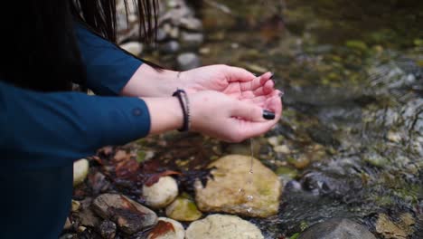 Mysterious-slow-motion-shot-of-a-woman-scooping-water-in-her-hands-at-a-forest-river