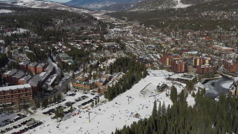 Aerial-drone-footage-of-the-Quicksilver-Super-Chair-lift,-skiers,-snowboarders,-and-a-pan-up-shot-of-Breckenridge,-Colorado