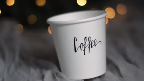 Christmas-coffee-paper-cup-on-a-cozy-bed-with-bokeh,-closeup