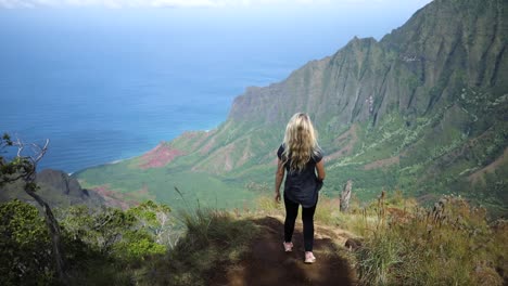 Young-woman-hiking-on-trail-in-Napali-Coast-State-Park-on-Kauai,-Hawaii