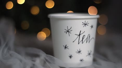 Christmas-tea-paper-cup-on-a-cozy-bed-with-bokeh-lights-in-the-background,-closeup