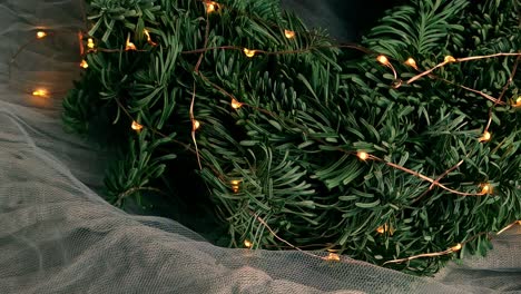 Looking-at-a-decorative-Christmas-wreath-made-of-pine-needles-and-fairy-lights-on-a-bed-of-thin,-transparent-cloth