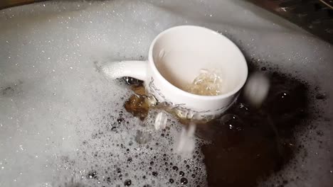 Schmutziges-Geschirr-Wird-In-Seifenwasser-Gewaschen,-Wobei-Ein-Teebecher-In-Die-Spüle-Fällt-Und-In-Zeitlupe-Spritzt