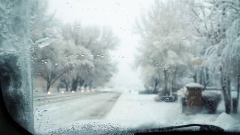 Inside-view-of-the-front-windshield-of-a-car-with-wet-snow-falling-onto-it-and-windshield-wipers-cleaning-it-off