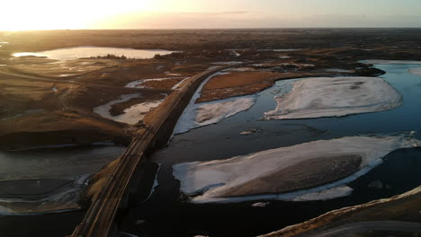 Drone-aerial-shot-on-Icelandic-landscape-at-sunset-on-a-lake-bridge-ice-and-snow