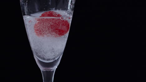 Slowmotion-shot-of-a-frozen-Raspberry-falling-into-a-glass-of-clear-water