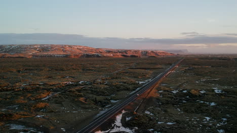 Drone-aerial-shot-on-typical-Iceland-landscape-with-a-car-passing-through,-red-sand,-red-mountains-and-snow