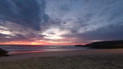 Time-lapse-of-sunrise-from-before-the-sun-appears-to-just-after-at-the-Arpoador-Devil's-beach-in-Rio-de-Janeiro,-Brazil,-with-intense-changing-colour-scheme-reflecting-in-the-incoming-waves