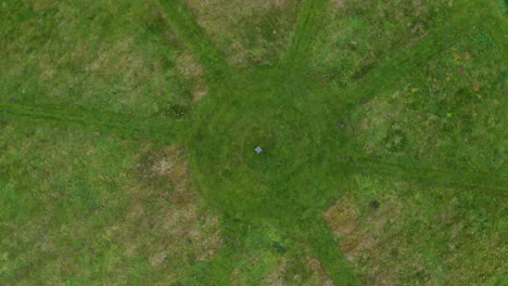 Aerial-descending-birds-eye-view-of-a-person-standing-in-a-circle-with-rays-formed-by-freshly-mown-grass