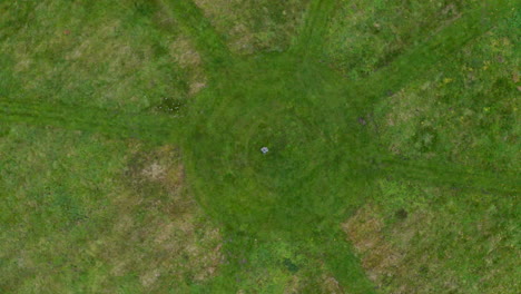 Aerial-ascending-reveal-shot-of-a-person-standing-in-a-circle-with-rays-formed-by-freshly-mown-grass