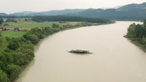 Aerial-pan:-Big-wooden-raft-floating-on-huge-river-Drava,-slovenia