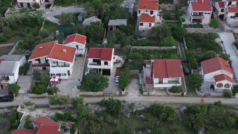 Two-people-walk-down-quiet-narrow-street-on-Adriatic-coast,-aerial