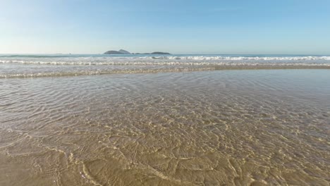 Time-lapse-of-low-angle-at-the-Atlantic-shore-with-clear-water-waves-coming-in-at-sunrise-with-the-islands-just-outside-of-Ipanema-beach-in-Rio-de-Janeiro-on-the-horizon