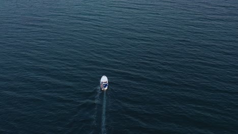 Aerial-drone-follows-small-white-boat-across-expanse-of-open-water