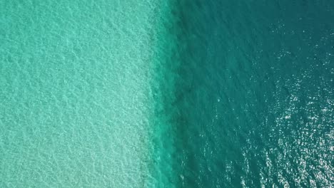 Aerial,-top-down,-drone-shot,-over-turquoise,-aqua-menthe-ocean,-overlooking-a-line-between-shallow,-lagoon-water-and-deeper-teal-colored-sea,-on-a-sunny-day,-in-Maldives