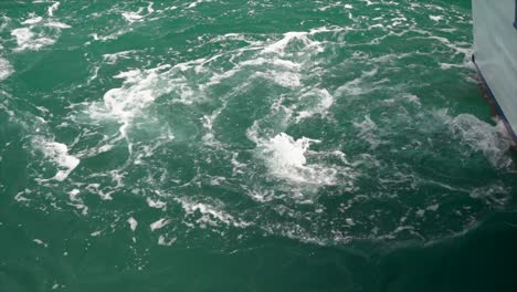 An-inboard-motor-churns-the-clear,-green-water-at-the-boat's-stern