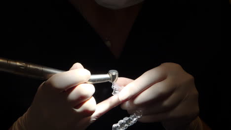 close-up-view-of-orthodontist-hands,-working-on-an-invisalign-aligner,-in-dark-setting-with-focus-light