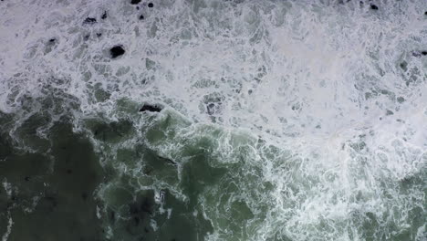 Texture-of-white-foam-swirls-in-grey-ocean-waves,-Aerial-Top-Down-Shot