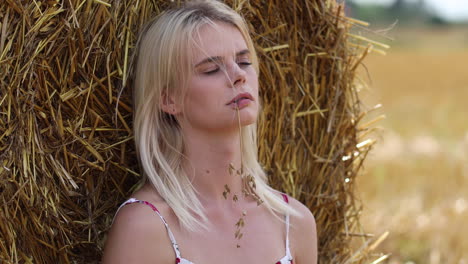 Sexy-blond-woman-with-wheat-corn-in-mouth-relaxing-in-front-of-hay-bale