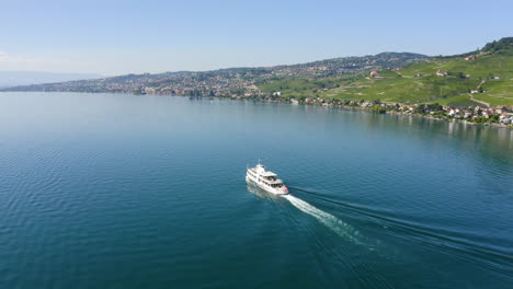 Ein-Touristenboot,-Das-Auf-Dem-Wunderschönen-Leman-see,-Lavaux-weinberg-In-Der-Schweiz-Mit-Der-Friedlichen-Stadt-Lausanne-Im-Hintergrund-Kreuzt---Luftaufnahme