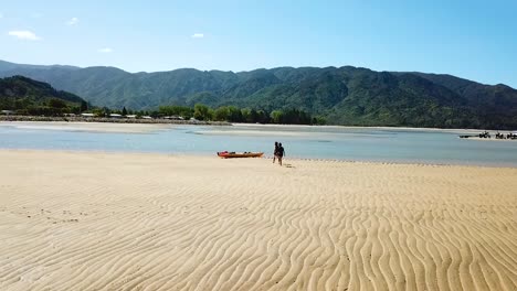 Slowmotion-Aerial-View-on-Two-People-Approaching-Kayak-in-Beach-Lagoon-on-Sandy-Bay,-New-Zealand