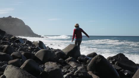Woman-carefully-walking-on-stone-coast-along-ocean