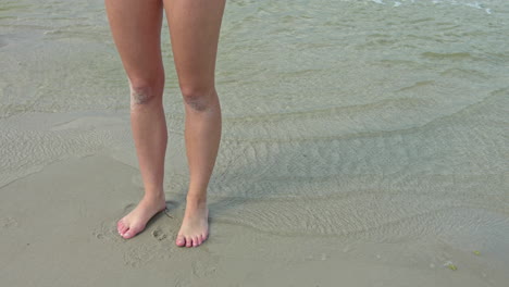 Static-shot-sportive-long-feminine-legs-standing-at-beach-sea-shore,slow-motion