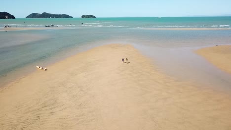 Luftzeitlupenansicht-Auf-Erstaunlicher-Strandlagune-Und-Zwei-Leute,-Die-Auf-Sand,-Sandige-Bucht,-Neuseeland-Gehen