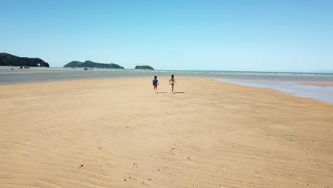 Slow-Motion-Tracking-Aerial-View-of-Couple-Running-on-Beach-in-Sandy-Bay-Lagoon