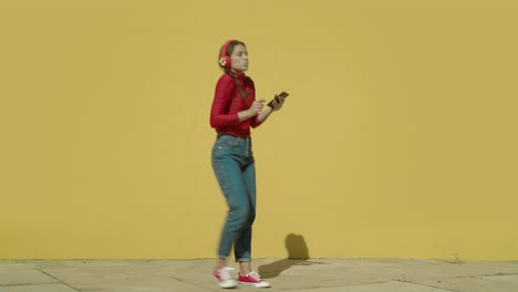 Young-Happy-Latin-Woman-wearing-red-shirt-and-jeans-and-red-converse-shoes-starts-dancing-with-a-yellow-background-wall-on-a-sunny-day-wide-angle-shot