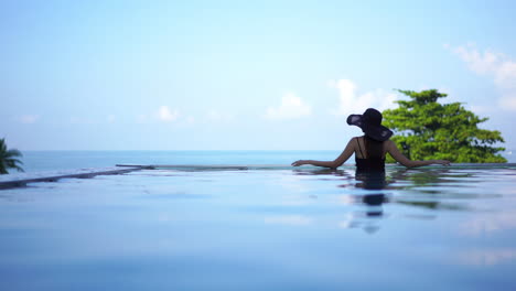 Woman-standing-in-swimming-pool-enjoying-sea-view