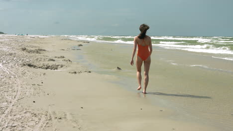 Static-wide-shot-of-sportive-woman-walking-on-beach-in-slow-motion