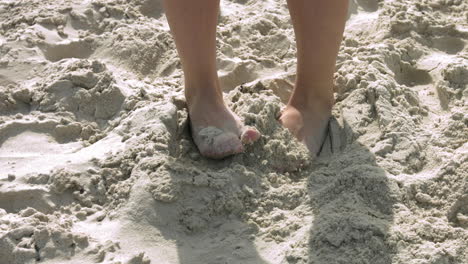 Low-angle-close-up-of-barefoot-feet-hiding-in-sand-at-beach,slow-motion