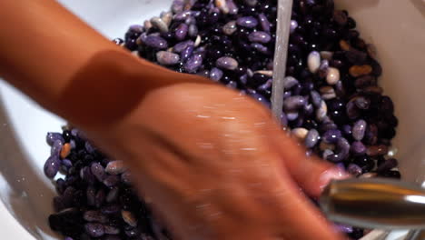 Rinsing-purple-black-beans-under-kitchen-tap-water,-Overhead-Closeup