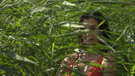 Pretty-young-woman-hiding-outdoor-behind-green-nature-plants-on-sunny-day,slow-motion