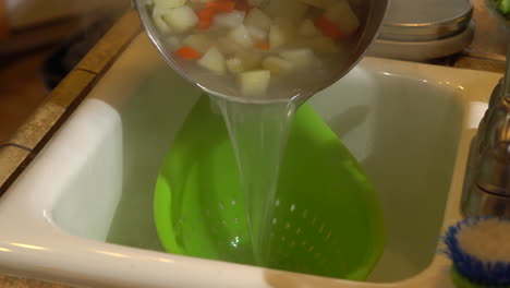 Pouring-pot-of-boiled-potatoes-and-carrots-into-green-strainer-to-drain,-CLOSEUP