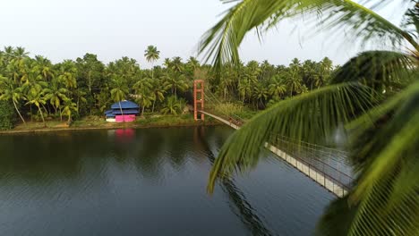 Aerial-flying-backwards-over-river-with-footbridge-in-Kochi,-Kerala