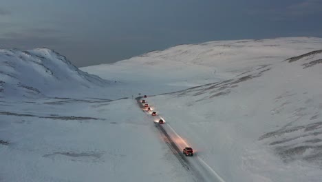 A-convoy-of-cars-driving-on-an-icy-road-towards-the-Nordkapp,-Norway-during-the-midwinter-solstice