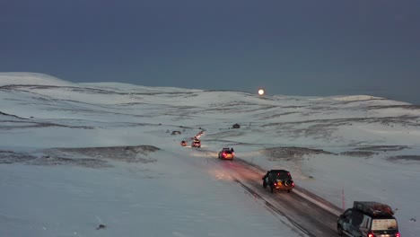 A-convoy-of-cars-driving-on-an-icy-road-towards-the-Nordkapp,-Norway-during-the-midwinter-solstice